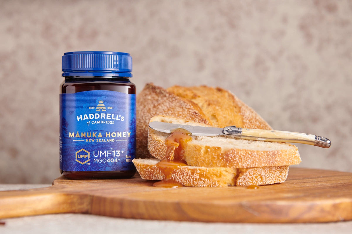 Miód manuka Haddrell's UMF 13⁺ obok kromek chleba posmarowanych miodem