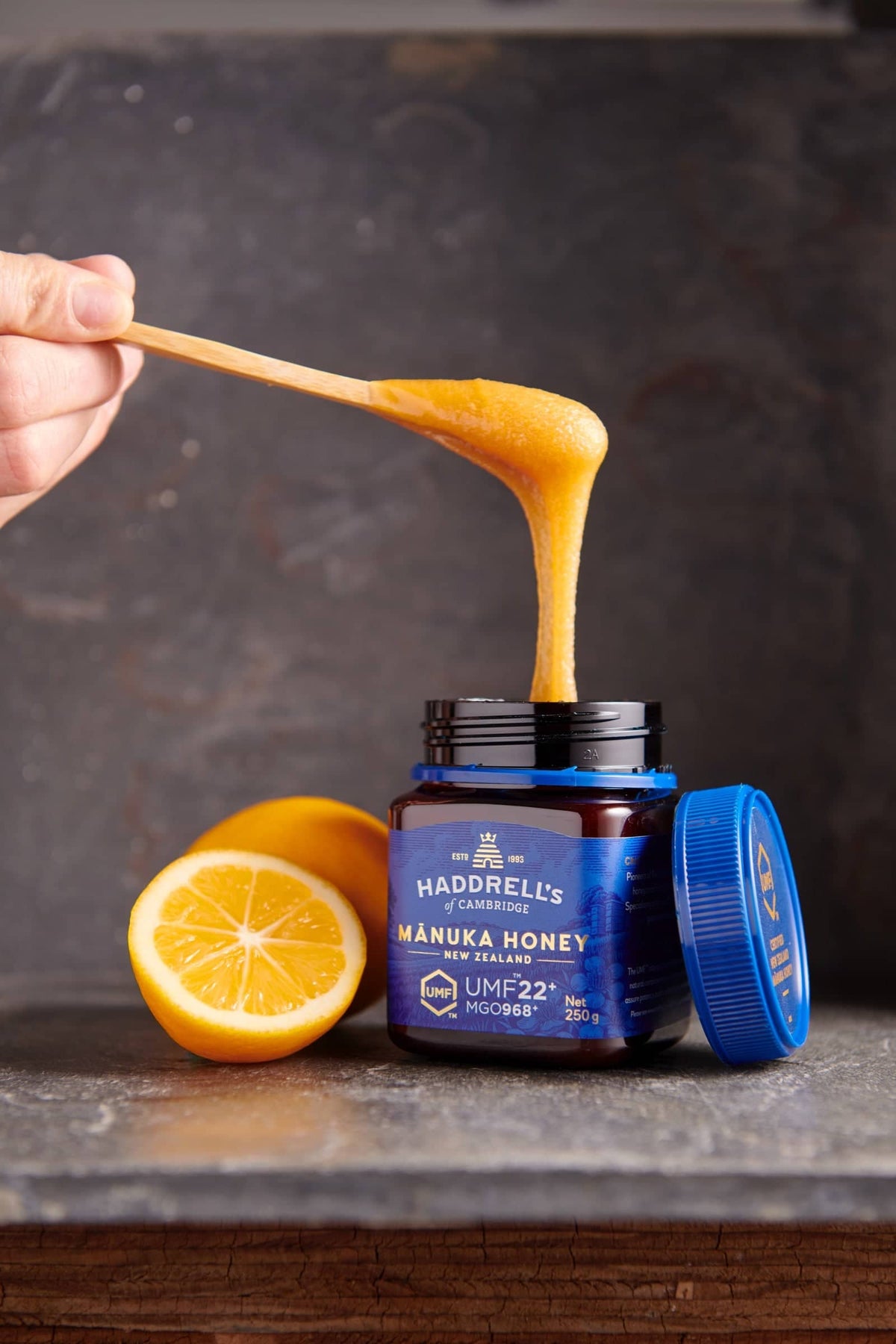 Łyżka miodu manuka nad słoikiem Haddrell's UMF 22⁺ 250 g, obok cytryna